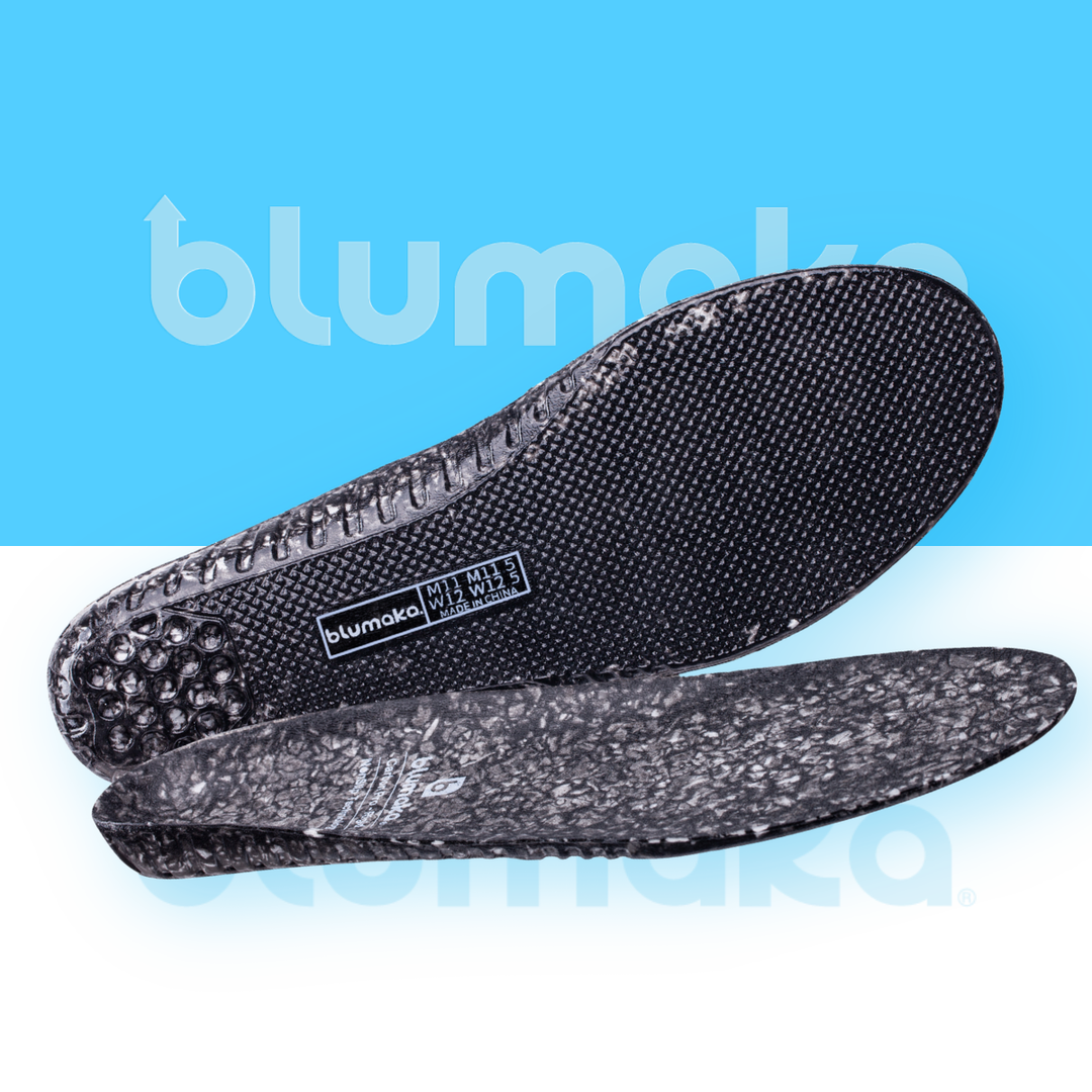 A pair of Blumaka Carbon Pro Rigid insoles on a pale blue background, one standing upright to show the black textured top surface and one lying flat to show the underside