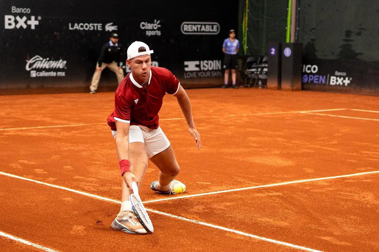 Danny Milavsky sliding for a low forehand on a clay court at a professional tournament