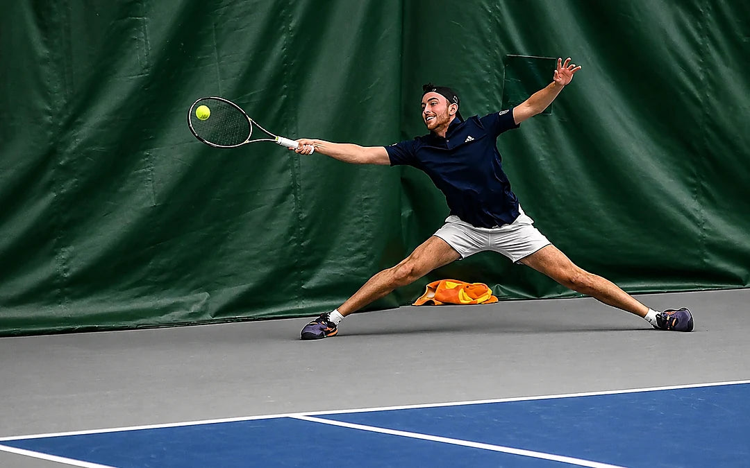 Jesús Soto lunging wide for a forehand on an indoor hard court at Principia College